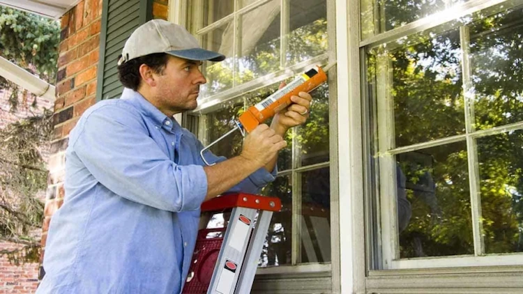 Seal the outside of an old window frame before winter like a professional with a ladder and caulking gun