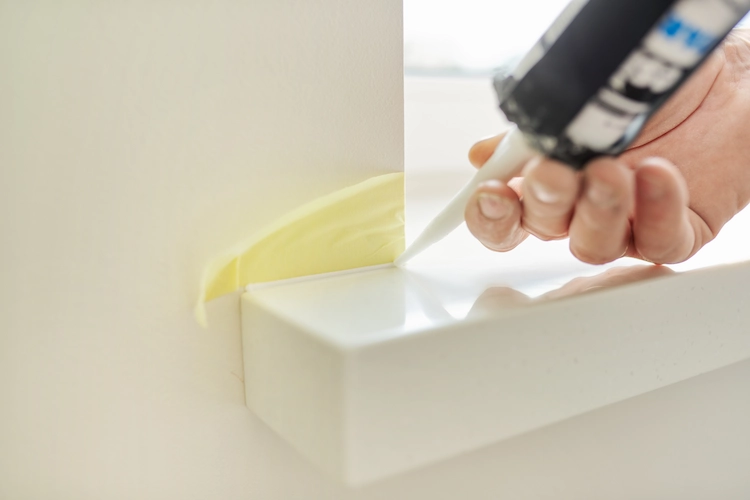 Protect the area between the window sill and the wall with painter's tape and apply sealant