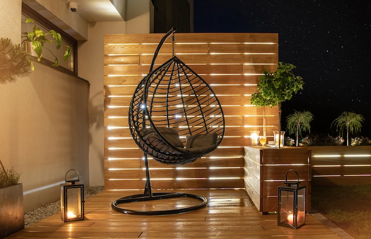 Stylish hanging chair on modern garden terrace with wooden paneling and outdoor lighting